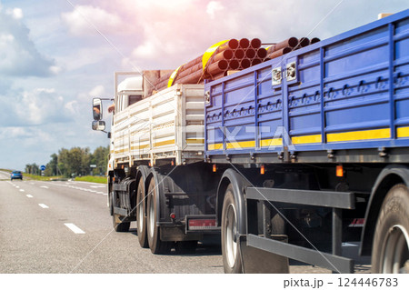 Transporting metal pipes on a semi-trailer truck along a highway in summer, industry. Transportation of metal products. Copy space for text, cloudy sky 124446783
