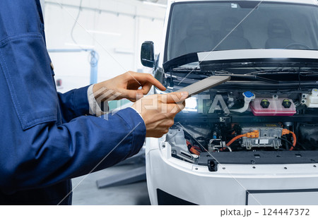 Serviceman with digital tablet next to electric van with open hood. Electric vehicles maintenance 124447372