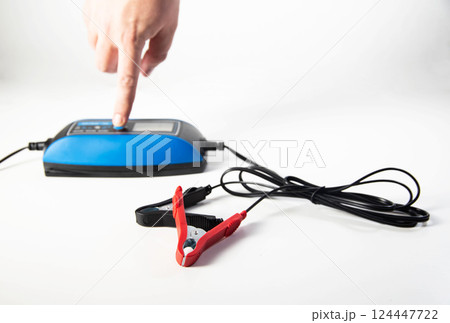 Modern pulse charger for AGM and EFB car batteries, close-up. Human hand switches modes Modern pulse charger for AGM and EFB car batteries, close-up. Human hand switches modes 124447722