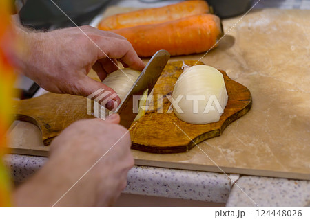 Men's hands slicing onions on wooden board in kitchen. Cooking with fresh vegetables. Healthy eating. Close-up 124448026