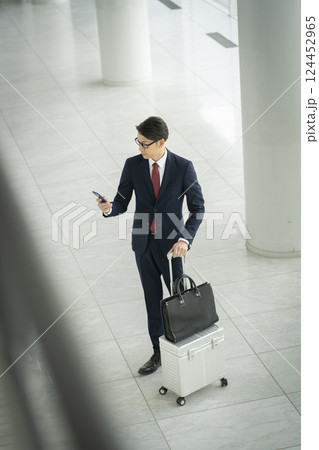 スマートフォンの画面を見るキャリーバッグを持った40代のビジネスマン 124452965