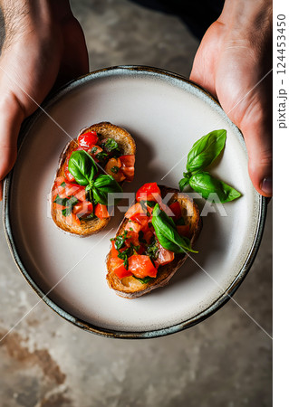 Chef holding plate with two slices of toasted bread topped with fresh tomatoes, basil, and seasonings, creating a classic italian bruschetta appetizer Chef holding plate with two slices of toasted bread topped with fresh tomatoes, basil, and seasonings, creating a classic italian bruschetta appetizer 124453450