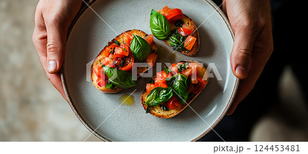 Chef holding plate with two slices of toasted bread topped with fresh tomatoes, basil, and seasonings, creating a classic italian bruschetta appetizer Chef holding plate with two slices of toasted bread topped with fresh tomatoes, basil, and seasonings, creating a classic italian bruschetta appetizer 124453481