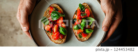 Chef holding plate with two slices of toasted bread topped with fresh tomatoes, basil, and seasonings, creating a classic italian bruschetta appetizer Chef holding plate with two slices of toasted bread topped with fresh tomatoes, basil, and seasonings, creating a classic italian bruschetta appetizer 124453482
