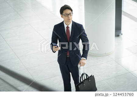スマートフォンとキャリーケースを持った40代のビジネスマン スマートフォンとキャリーケースを持った40代のビジネスマン 124453760