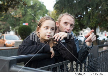 Cheerful daughter child girl and her father together looking at something and pointing.  124454870
