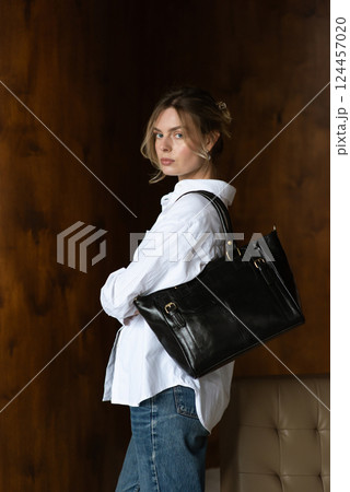 A girl in a white shirt and blue jeans is posing with a black shopper bag. A girl in a white shirt and blue jeans is posing with a black shopper bag. 124457020