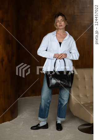 A girl in a white shirt blue jeans and loafers is posing with a black shopper bag. A girl in a white shirt blue jeans and loafers is posing with a black shopper bag. 124457022