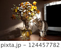A beautiful striped cat stands on a table near a bouquet of flowers, looking with interest 124457782