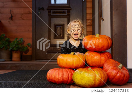 smiling girl is sitting next to pumpkins near the door of the house. halloween decor. smiling girl is sitting next to pumpkins near the door of the house. halloween decor. 124457818