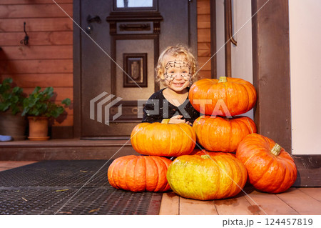 a child celebrates Halloween. The porch and front door of the house are decorated with pumpkins. Halloween decor 124457819