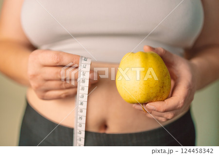 Woman holding yellow apple and measuring tape, healthy eating concept Woman holding yellow apple and measuring tape, healthy eating concept 124458342