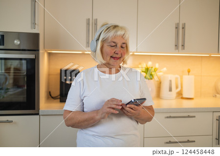 Senior woman listening to music in the kitchen, enjoying the moment 124458448
