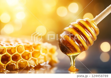 Golden honey drips from a honey dipper above honeycomb against a dark background Golden honey drips from a honey dipper above honeycomb against a dark background 124458789