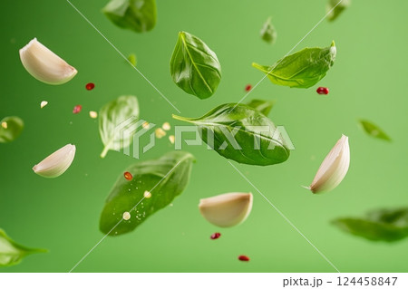 Vibrant green leaves, garlic cloves, and chili peppers swirl through the air, showcasing an energetic burst of flavors 124458847