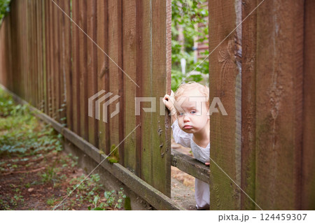 bored child looks through a hole in a brown fence. Summer day. bored child looks through a hole in a brown fence. Summer day. 124459307