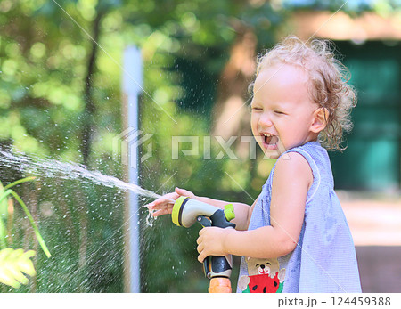 little girl cheerfully splashes water from a watering hose on a sunny summer day 124459388
