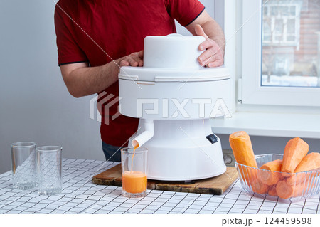 faceless man squeezes carrot juice in a white professional juicer. 124459598