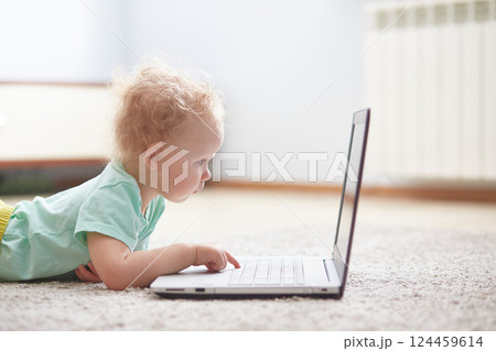 small child at a computer lying on a carpet in a living room. 124459614