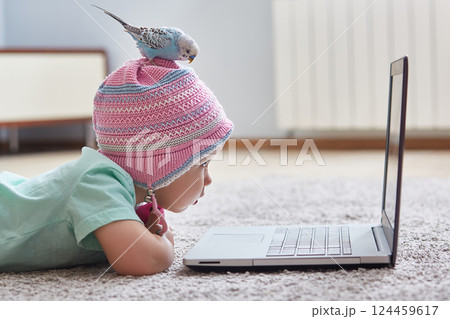 Funny Quarantine Moments. A parrot sits on the head of a child in a hat. The girl looks at her laptop. The concept of learning at home during quarantine and self-isolation from coronavirus infection Funny Quarantine Moments. A parrot sits on the head of a child in a hat. The girl looks at her laptop. The concept of learning at home during quarantine and self-isolation from coronavirus infection 124459617