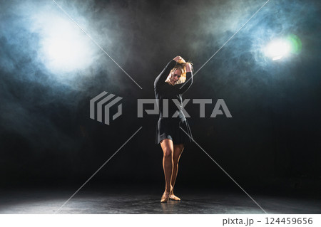 Contemporary woman dancer posing on black background with smoke. Adult female artist performer dancing with expression. Modern ballerina dancing in darkness. Passion dance in dark. Flexibility balance Contemporary woman dancer posing on black background with smoke. Adult female artist performer dancing with expression. Modern ballerina dancing in darkness. Passion dance in dark. Flexibility balance 124459656