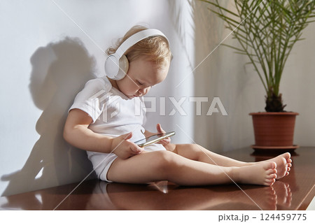 small child uses a mobile phone with headphones on his head. 124459775