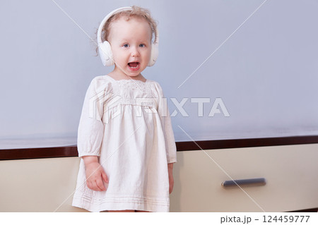 Little girl sings a song in her headphones. Light background with space for text 124459777