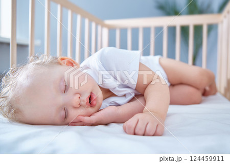 Baby sleeps in baby wooden crib for newborns. A spacious, bright room with a date palm tree in the background. 124459911