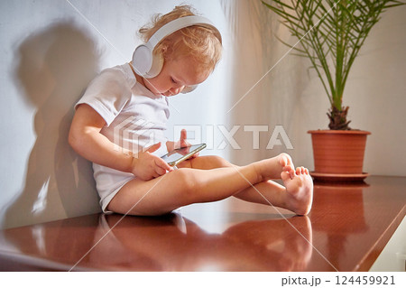 small child uses a mobile phone with headphones on his head. small child uses a mobile phone with headphones on his head. 124459921