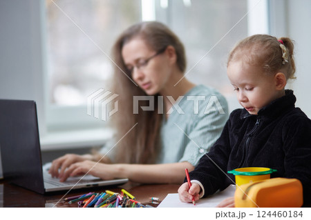A girl draws with pencils while working as a freelancer's mother. The concept of working at home and taking care of the family A girl draws with pencils while working as a freelancer's mother. The concept of working at home and taking care of the family 124460184