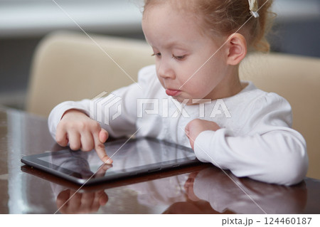 A little surprised girl is playing with a digital wireless tablet computer at home. The concept of a child and electronic devices. The concept of education and learning ability. 124460187