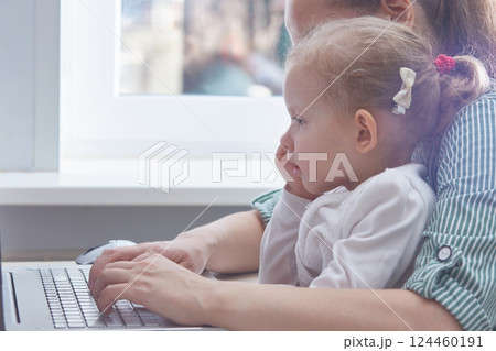 The child is in the arms of a mother working on a laptop at home. The concept of freelancing and working from home with children. Copy space. 124460191