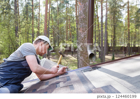 The master attaches a soft tile roof to the roof of a country house. The master attaches a soft tile roof to the roof of a country house. 124460199