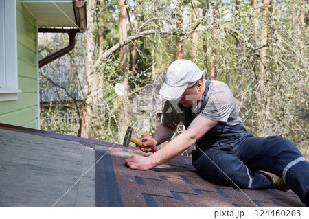 A worker installs a soft roof on the roof of a country house. Made of modified bitumen and stone chips based on fiberglass. 124460203