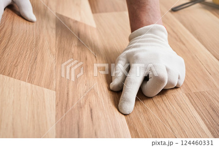Installing laminated floor, detail on man hands in white gloves fitting wooden tile Installing laminated floor, detail on man hands in white gloves fitting wooden tile 124460331