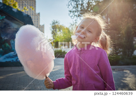 Curly-haired girl enthusiastically eats cotton candy. The concept of a family of children and happiness with children. 124460639
