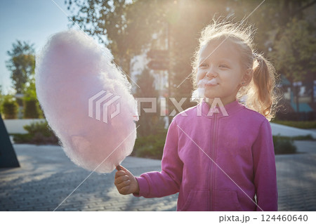 Curly-haired girl enthusiastically eats cotton candy. The concept of a family of children and happiness with children. 124460640
