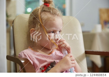 A sick girl breathes with a nebulizer inhaler at home during her illness. Lifestyle. 124460654