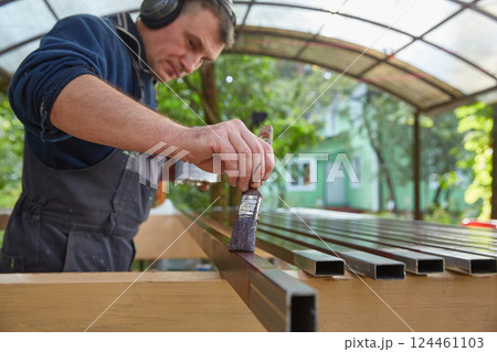 A faceless man draws iron pipes against the background of his house on a sunny summer day in his garden. Focus on the brush. Copy space 124461103