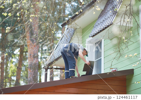 View from the window of the cottage. A person working on the roof installs a soft roof. View from the window of the cottage. A person working on the roof installs a soft roof. 124461117