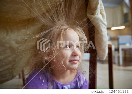 A child at home plays in a house built from a blanket. 124461131
