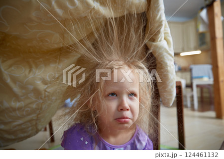 Sad girl is sitting at home with electrified hair sticking up. Children's games for preschoolers at home. 124461132
