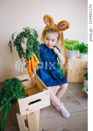 Cute little child girl wearing bunny ears on Easter day and eating sweet carrot Cute little child girl wearing bunny ears on Easter day and eating sweet carrot 124461170