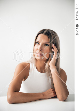 Woman with long hair poses thoughtfully against a minimalistic background in bright lighting 124461182