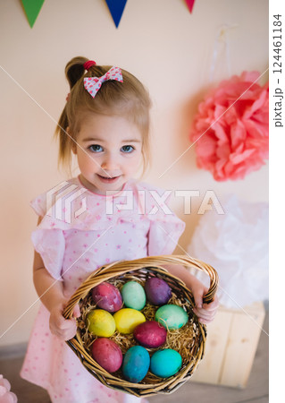 Cute little girl wearing pink dress holding basket with painted Easter eggs 124461184