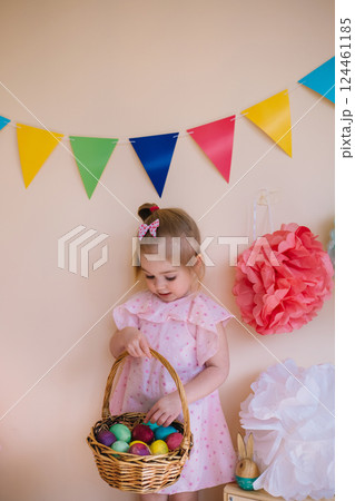Cute little girl wearing pink dress holding basket with painted Easter eggs 124461185