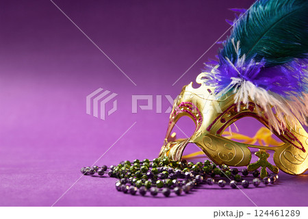 The concept of Masquerade disguise. Purple background with copy space. Mask with green and purple beads and sequins. The concept of Masquerade disguise. Purple background with copy space. Mask with green and purple beads and sequins. 124461289