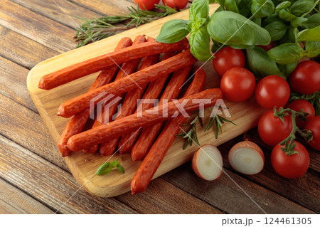 Kabanos sausages with basil and tomatoes on a cutting board. 124461305