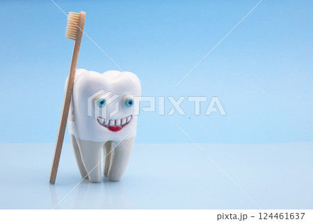 Smiling Tooth. A whimsical tooth figure with eyes and a smile, accompanied by a wooden toothbrush 124461637