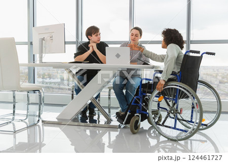 Teamwork brainstorm. Diverse multiracial colleagues woman in chair for people with disability working together. Group of people sitting in creative office discussing business. Young professional team 124461727